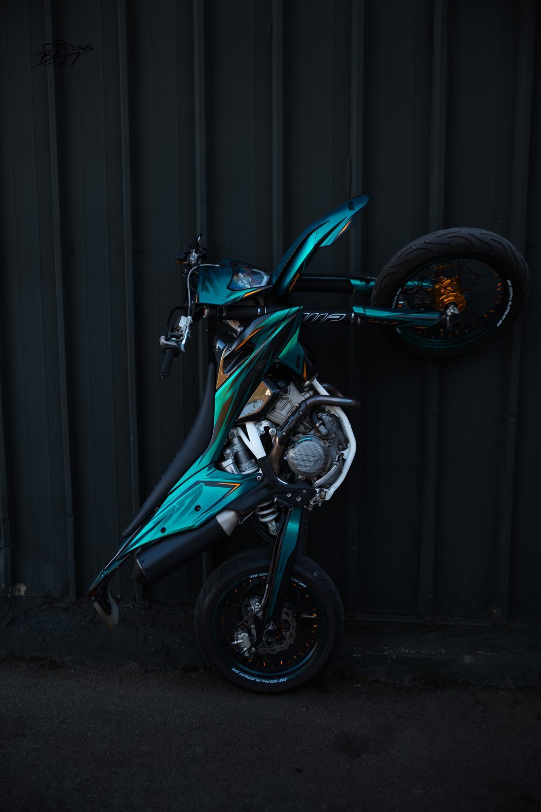 Supermotard turquoise dressée contre un mur sombre